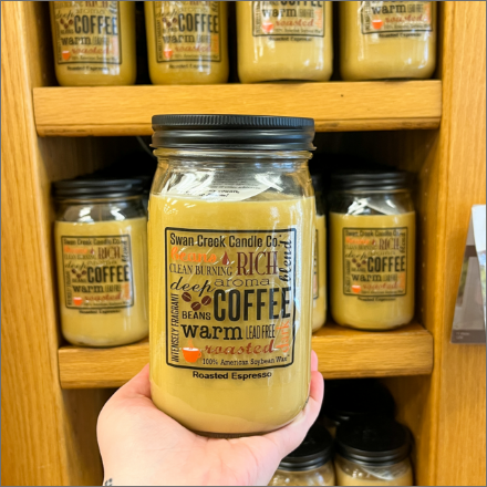 Coffee sented candle held in front of wooden shelves